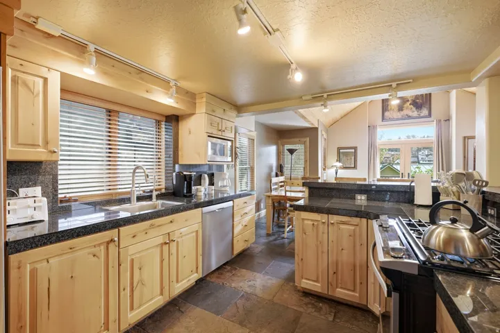 Wood-finish cabinetry, dark stone countertops, stainless steel appliances, and slate flooring
