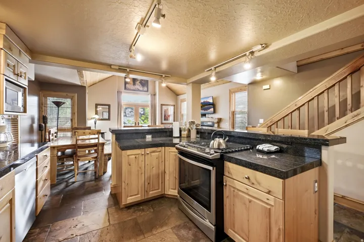 Kitchen featuring wood cabinetry, dark countertops, a stainless steel range, and slate flooring