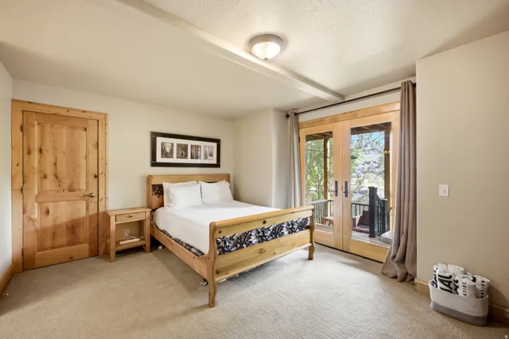 Carpeted flooring, natural wood door, wood-finish French doors, wood beam ceiling detail, and ceiling-mounted light fixture