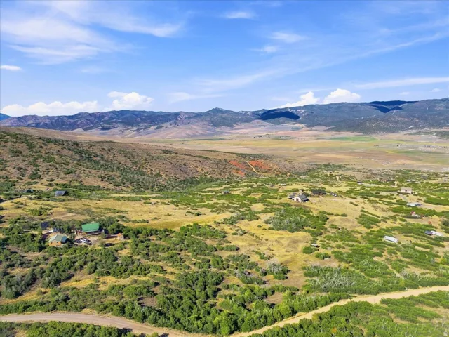 Expansive rural landscape featuring multiple structures, rolling hills, and distant mountains under a blue sky