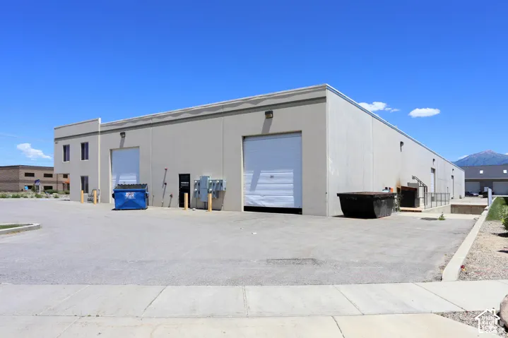 Large commercial building featuring multiple roll-up doors, extensive paved lot, and a mountain backdrop