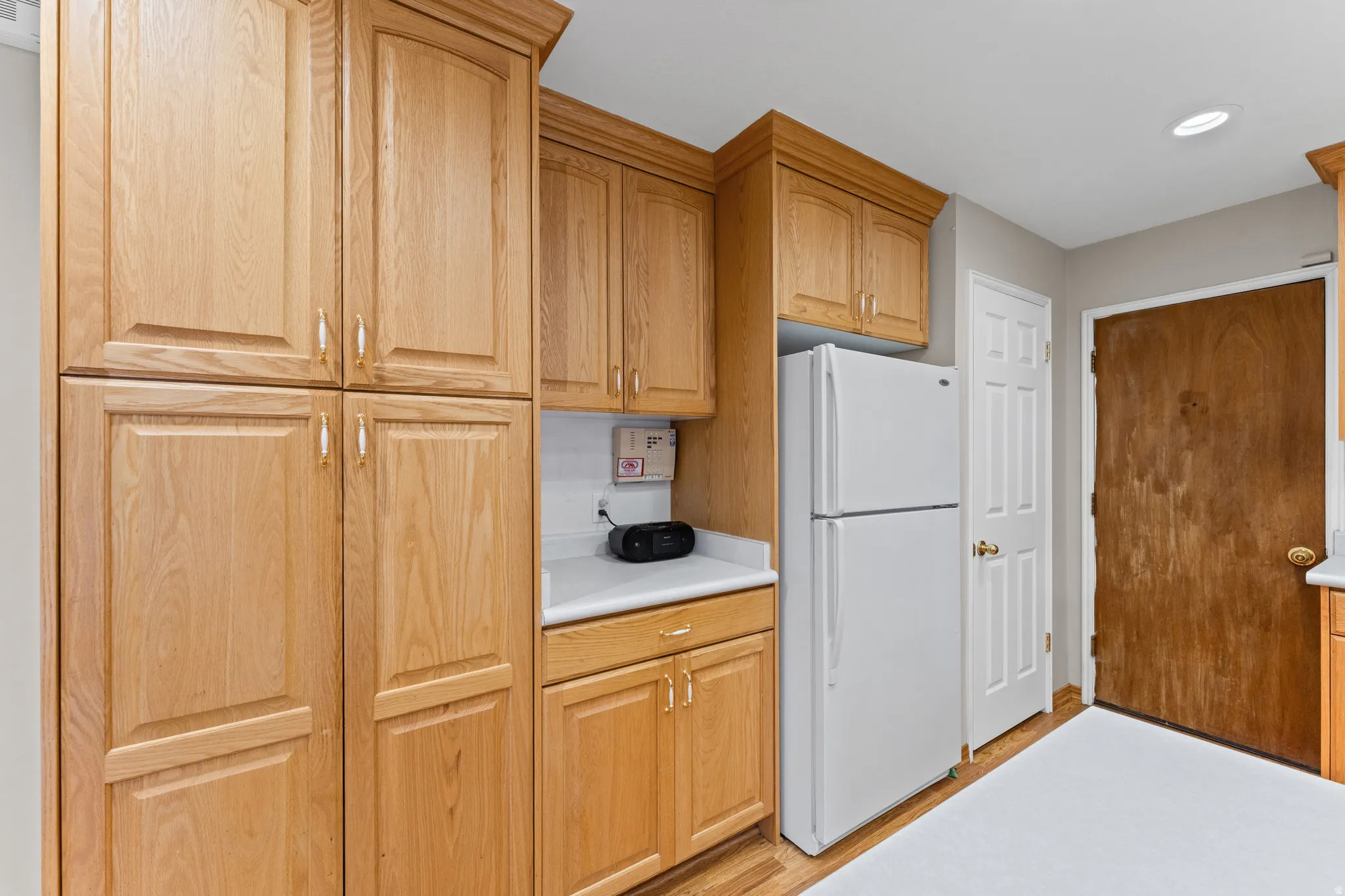 Wood-finish cabinetry with crown molding, white countertop, white refrigerator, and recessed lighting
