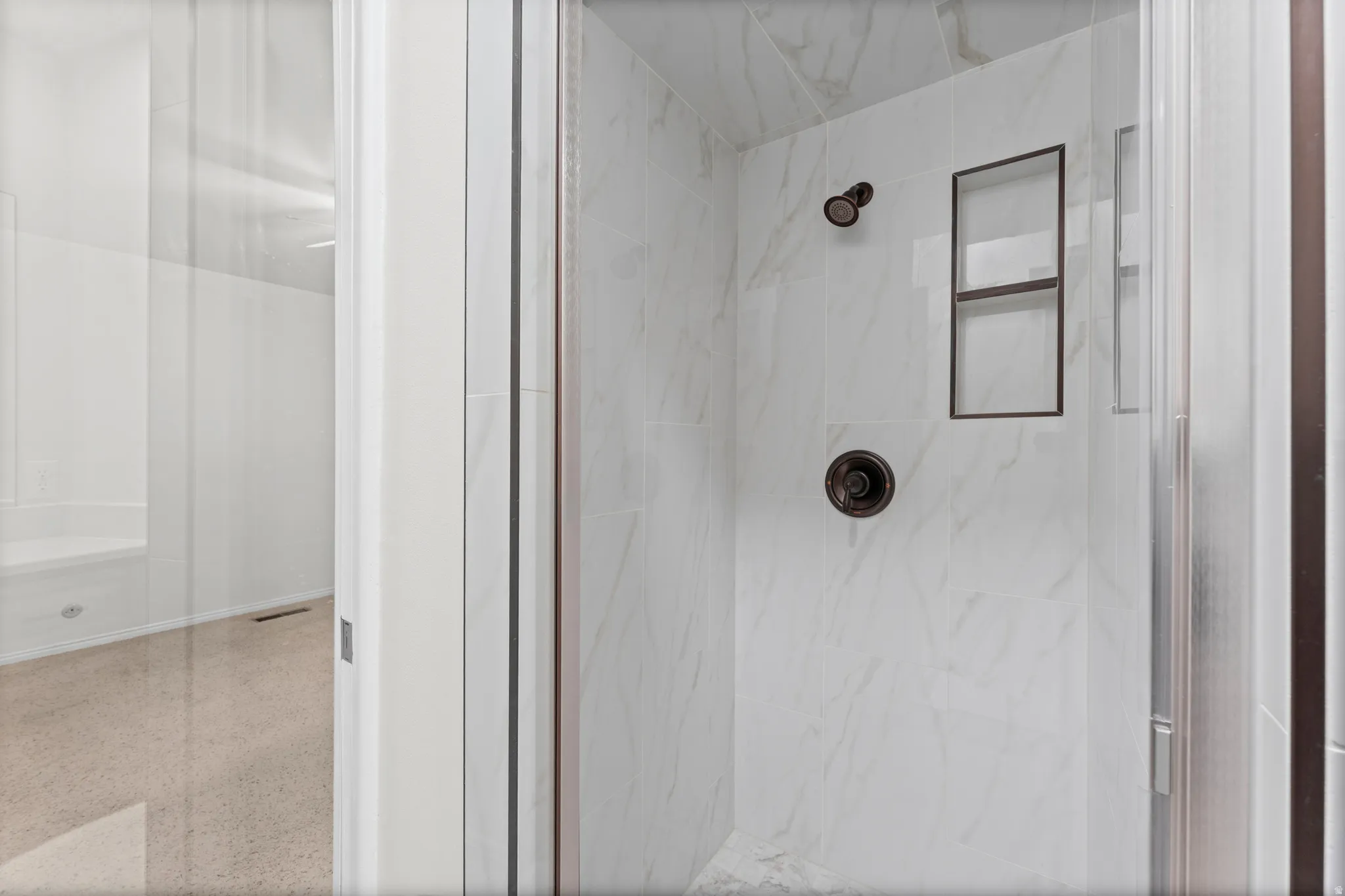 Marble-look shower with a dark bronze rainfall showerhead, matching control knob, and a built-in recessed shelf
