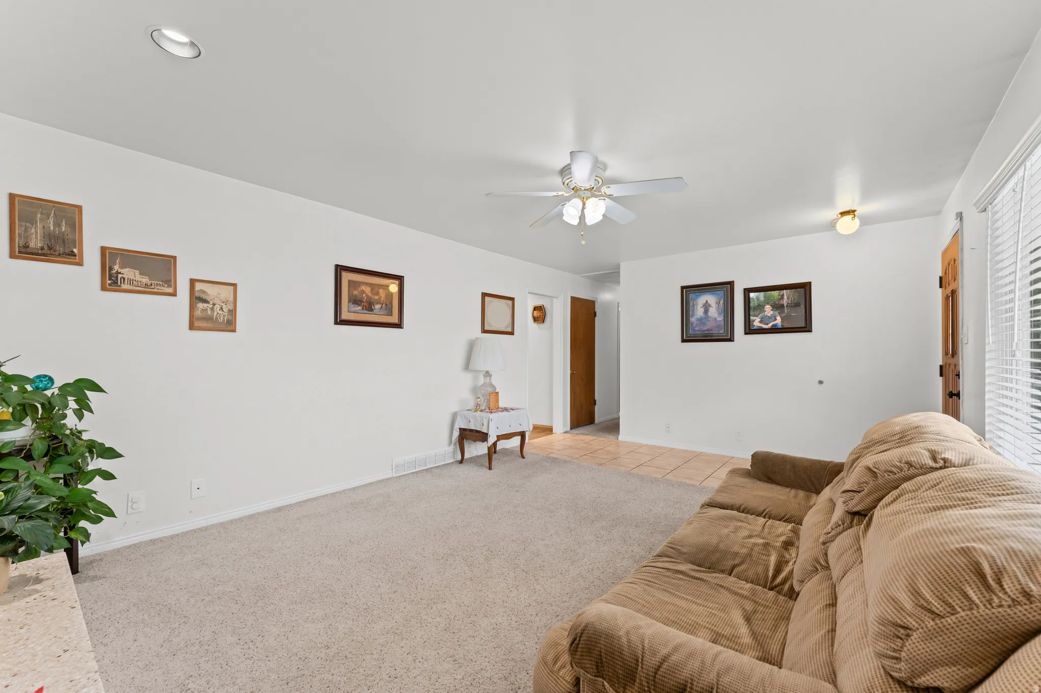 Carpeted living area with white walls and a ceiling fan