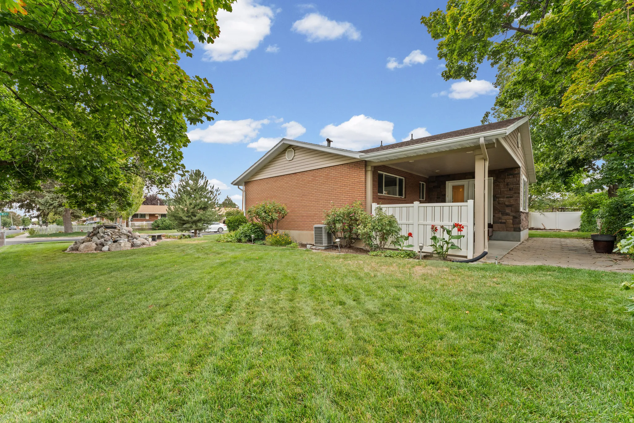Expansive lawn area, mature trees, brick exterior, covered patio, and stone siding accents