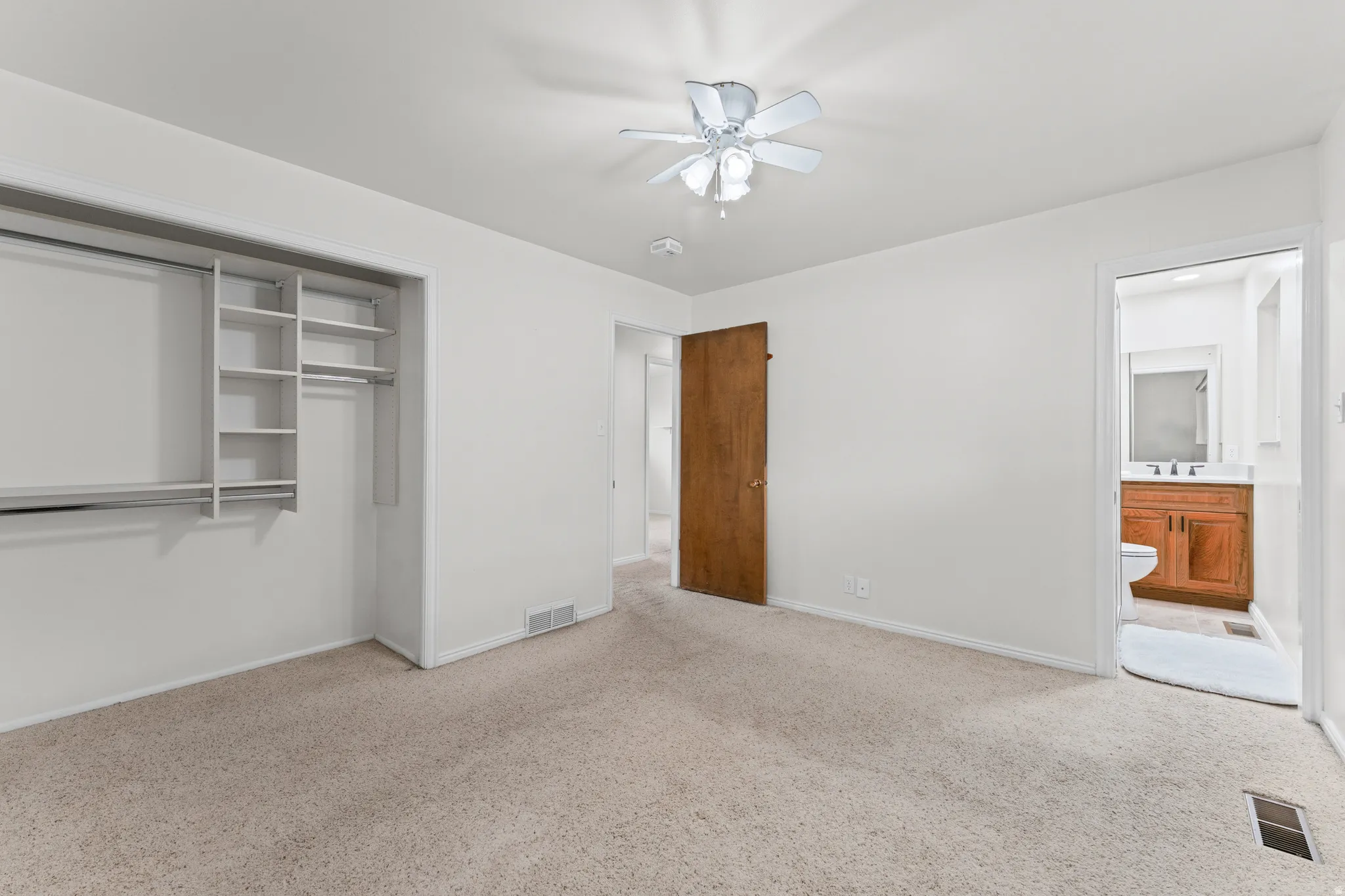 Neutral-toned carpeting, ceiling fan with integrated lighting, and a wood-finish door