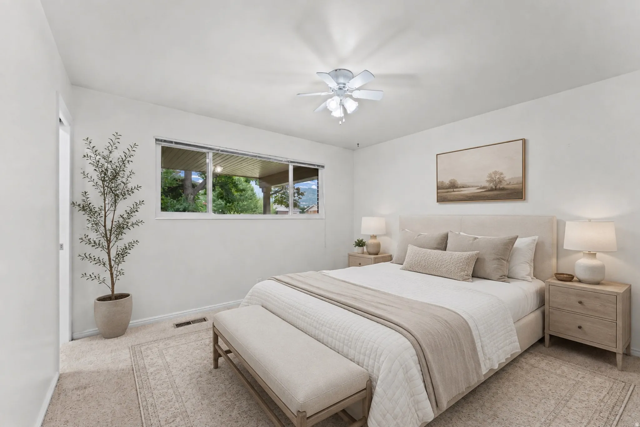 Carpet flooring, white painted walls, window with outdoor scenery, flush mount ceiling fan, and a light-colored headboard