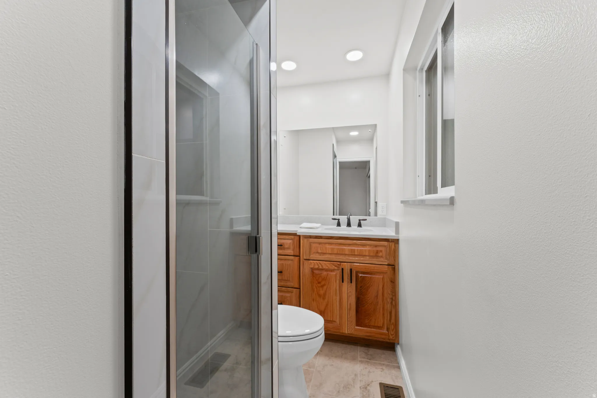 Glass-enclosed shower with subway tile surround, wood-finish vanity with countertop, and recessed lighting