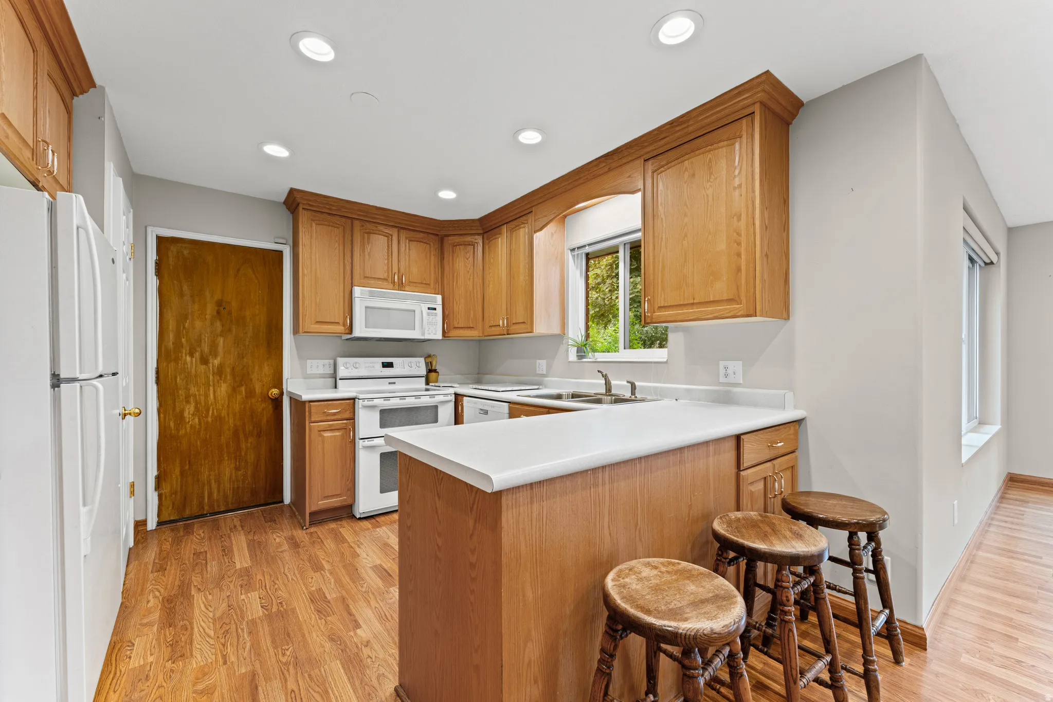 Kitchen featuring wood-finish flooring, recessed lighting, wood cabinetry, built-in white appliances, and a window above the sink