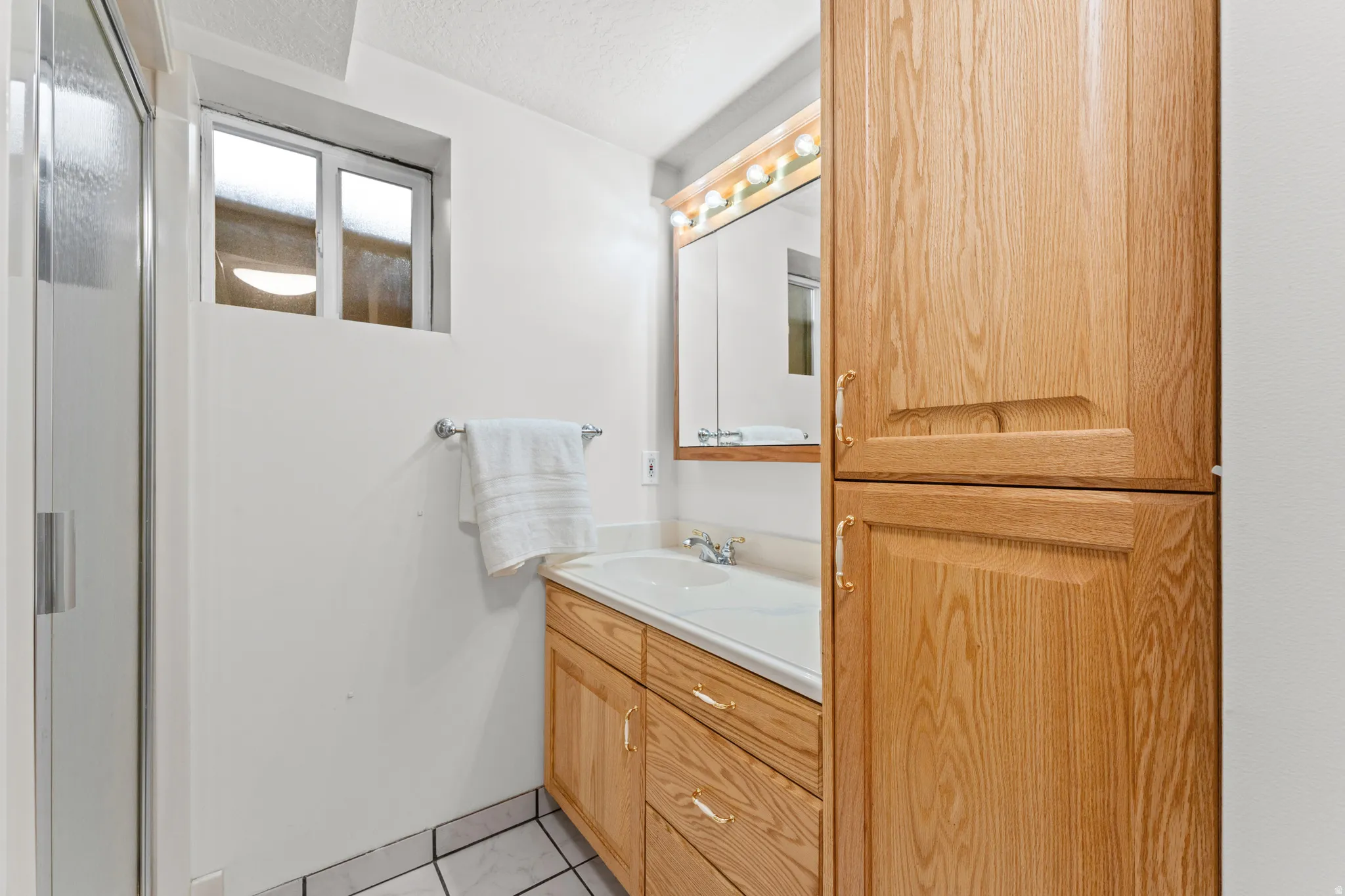 Wood-finish cabinetry, integrated vanity sink, mirrored medicine cabinet, tile flooring, and a glass-enclosed shower