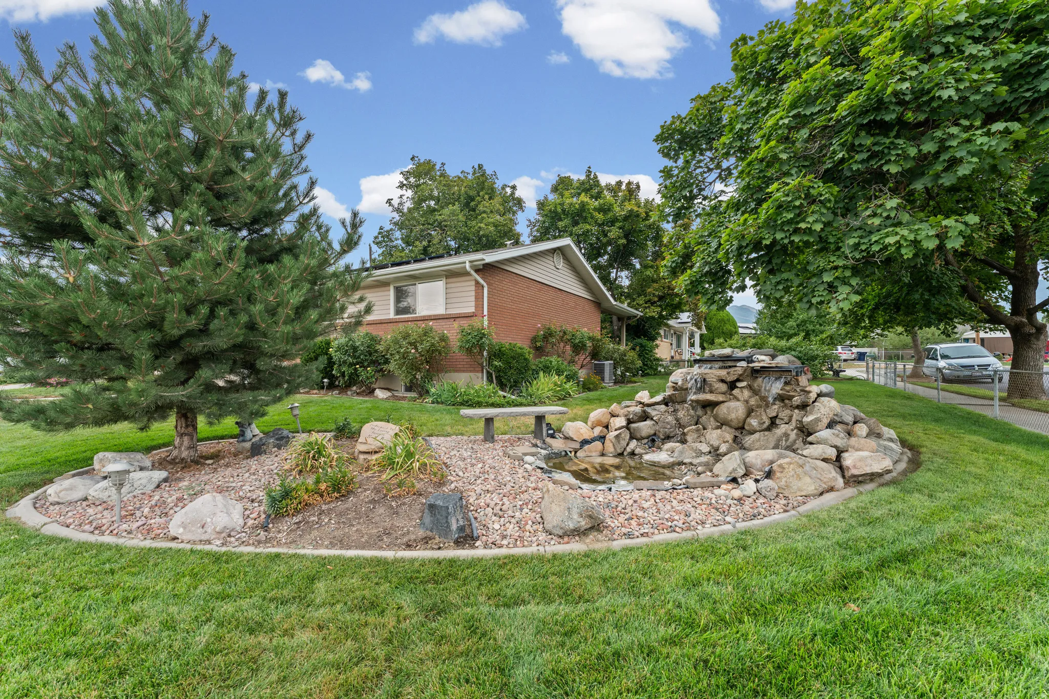 Landscaped yard featuring a water feature with rock accents, mature trees, and a stone bench