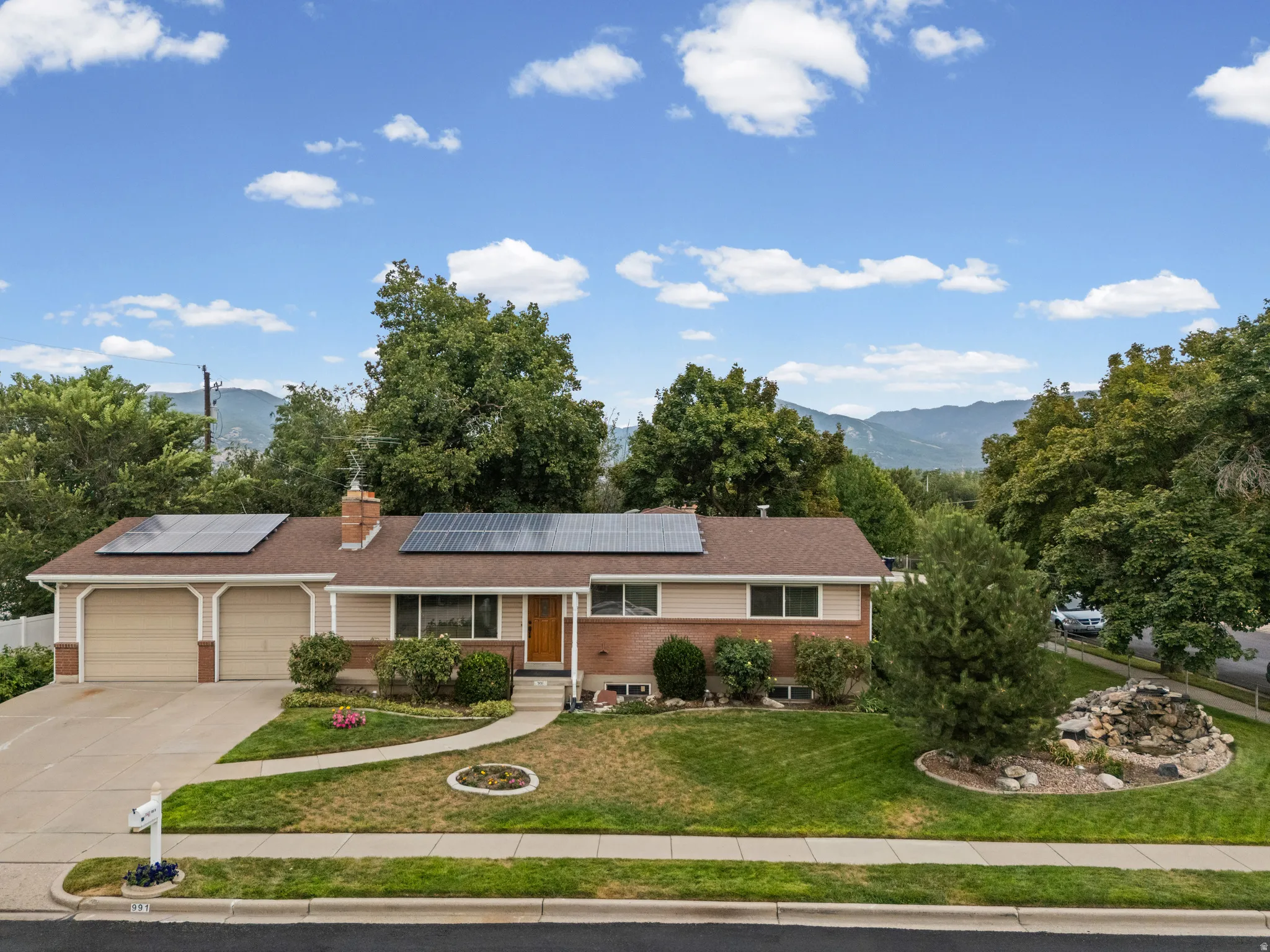 Front exterior featuring a two-car garage, solar panels, a manicured lawn, and a stone water feature