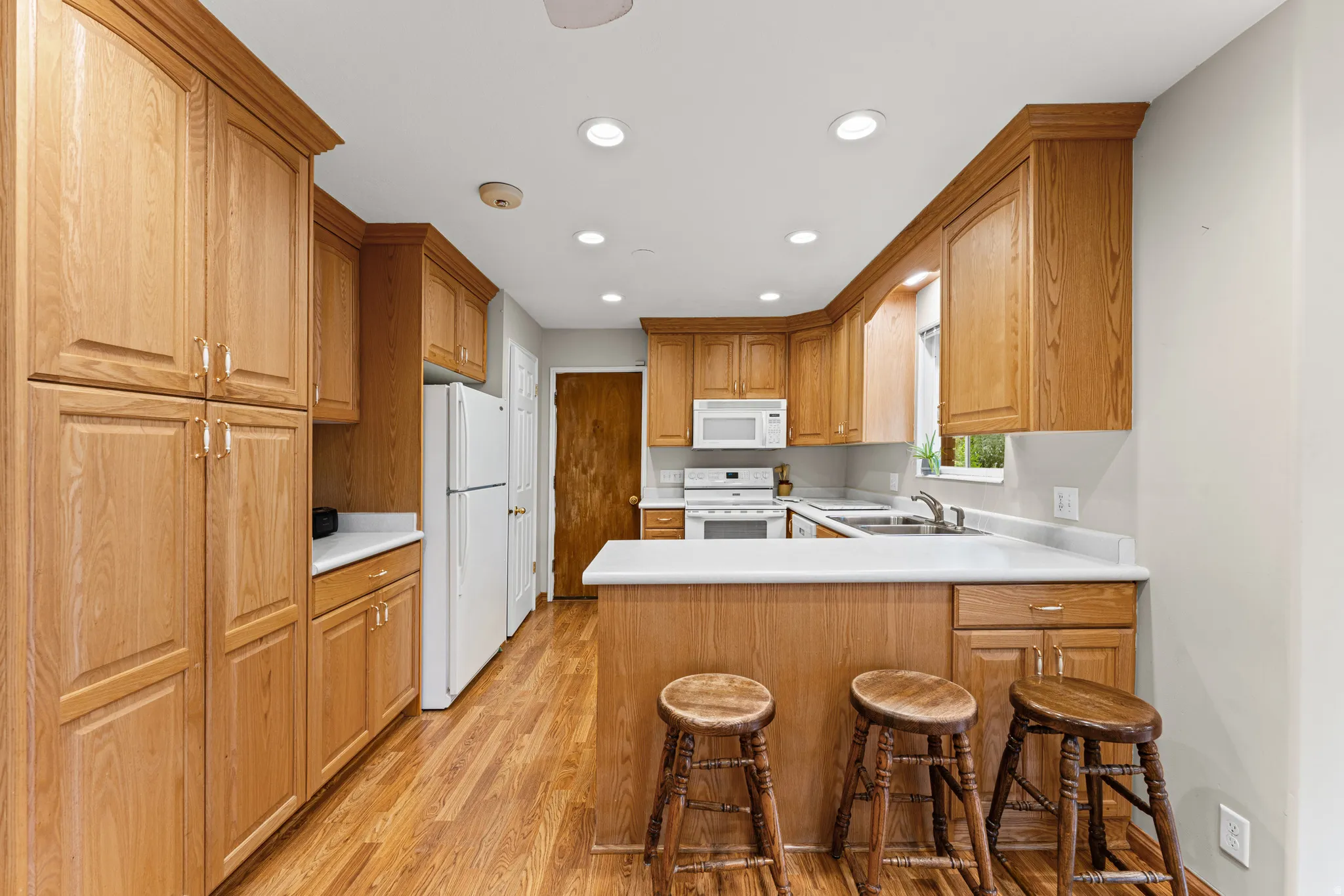 Kitchen featuring wood-finish cabinetry, white countertops, stainless steel sink, and wood-finish flooring