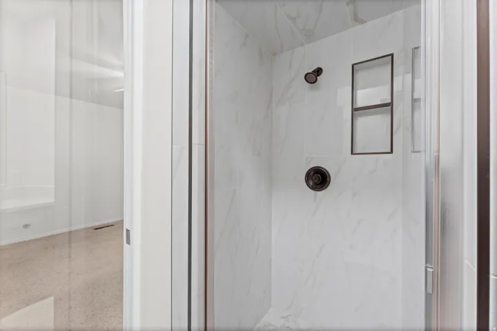 Marble-look shower with a dark bronze rainfall showerhead, matching control knob, and a built-in recessed shelf