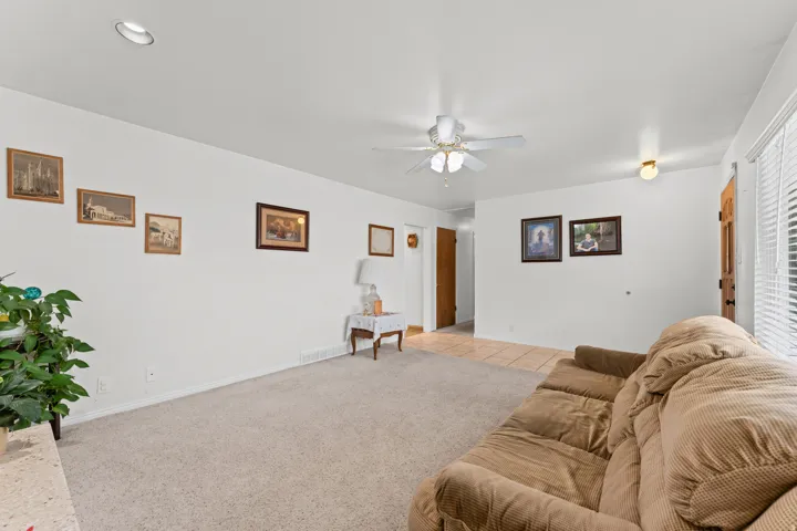 Carpeted living area with white walls and a ceiling fan