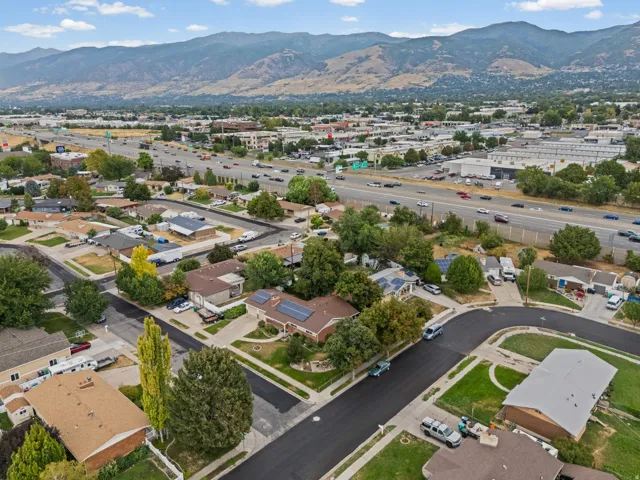 Residential neighborhood with paved streets and mature trees, featuring distant mountains and a multi-lane highway