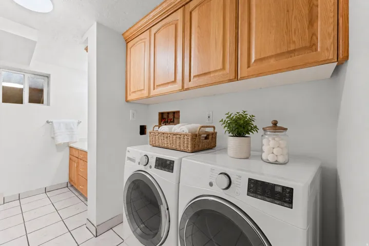 Laundry area featuring light wood-finish cabinetry, tile flooring, and a compact window