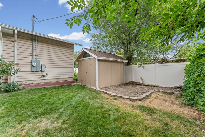 Rear yard featuring a storage shed, a white privacy fence, and a grassy area