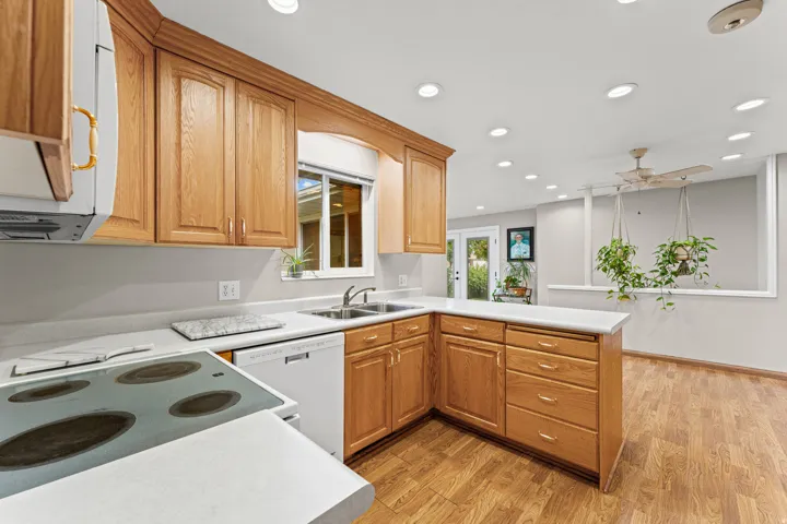 Kitchen with wood-finish cabinetry, light-toned countertops, a stainless steel double sink, and integrated white appliances
