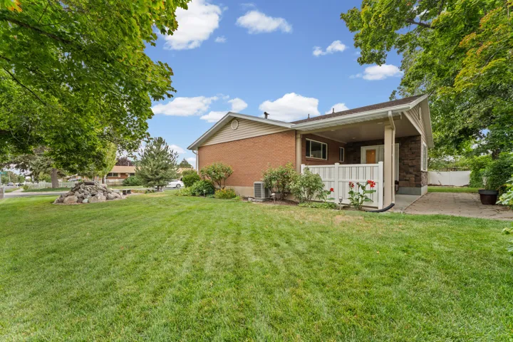 Expansive lawn area, mature trees, brick exterior, covered patio, and stone siding accents