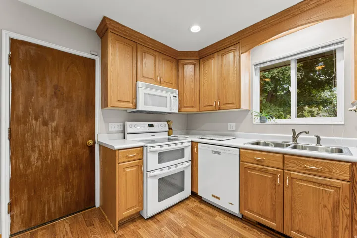 Kitchen featuring wood-finish flooring, wood cabinetry with gold-tone hardware, white countertops, and a double-basin stainless steel sink