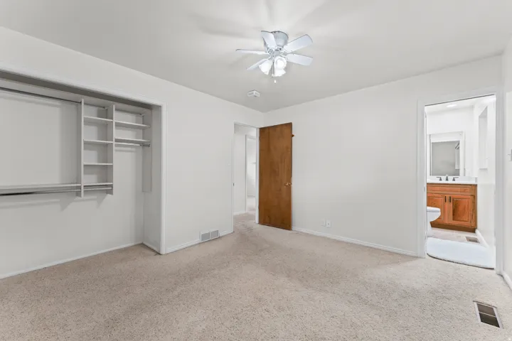 Neutral-toned carpeting, ceiling fan with integrated lighting, and a wood-finish door