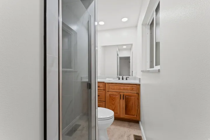 Glass-enclosed shower with subway tile surround, wood-finish vanity with countertop, and recessed lighting
