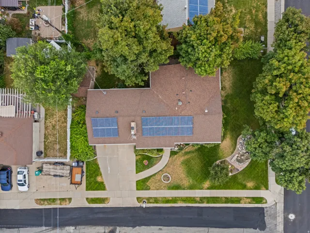Roof-mounted solar panels, paved driveway, concrete walkway, established trees, and front yard landscaping
