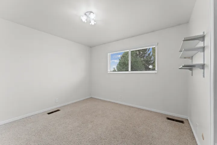 Neutral wall paint, carpet flooring, a window with blinds, and built-in shelving