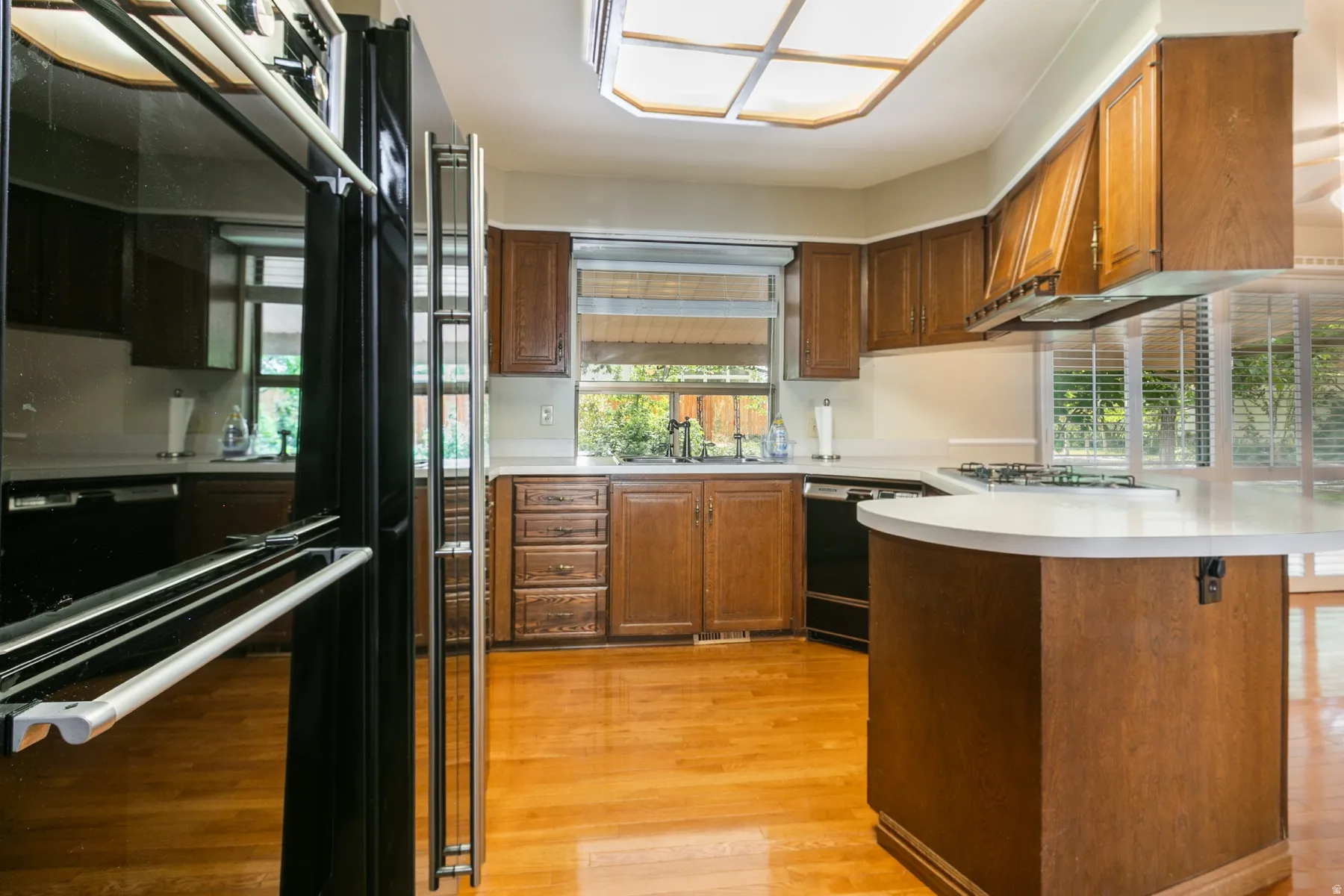 Chef's kitchen showcasing rich wood cabinetry, stainless steel appliances including a professional-style range, white quartz countertops, a curved island with seating, hardwood flooring, and abundant natural light from multiple windows and skylights