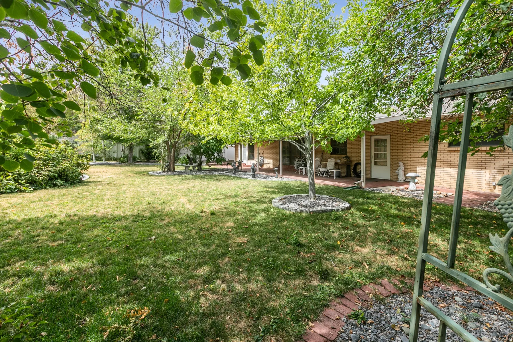 Expansive backyard featuring a manicured lawn, established trees, and a brick patio