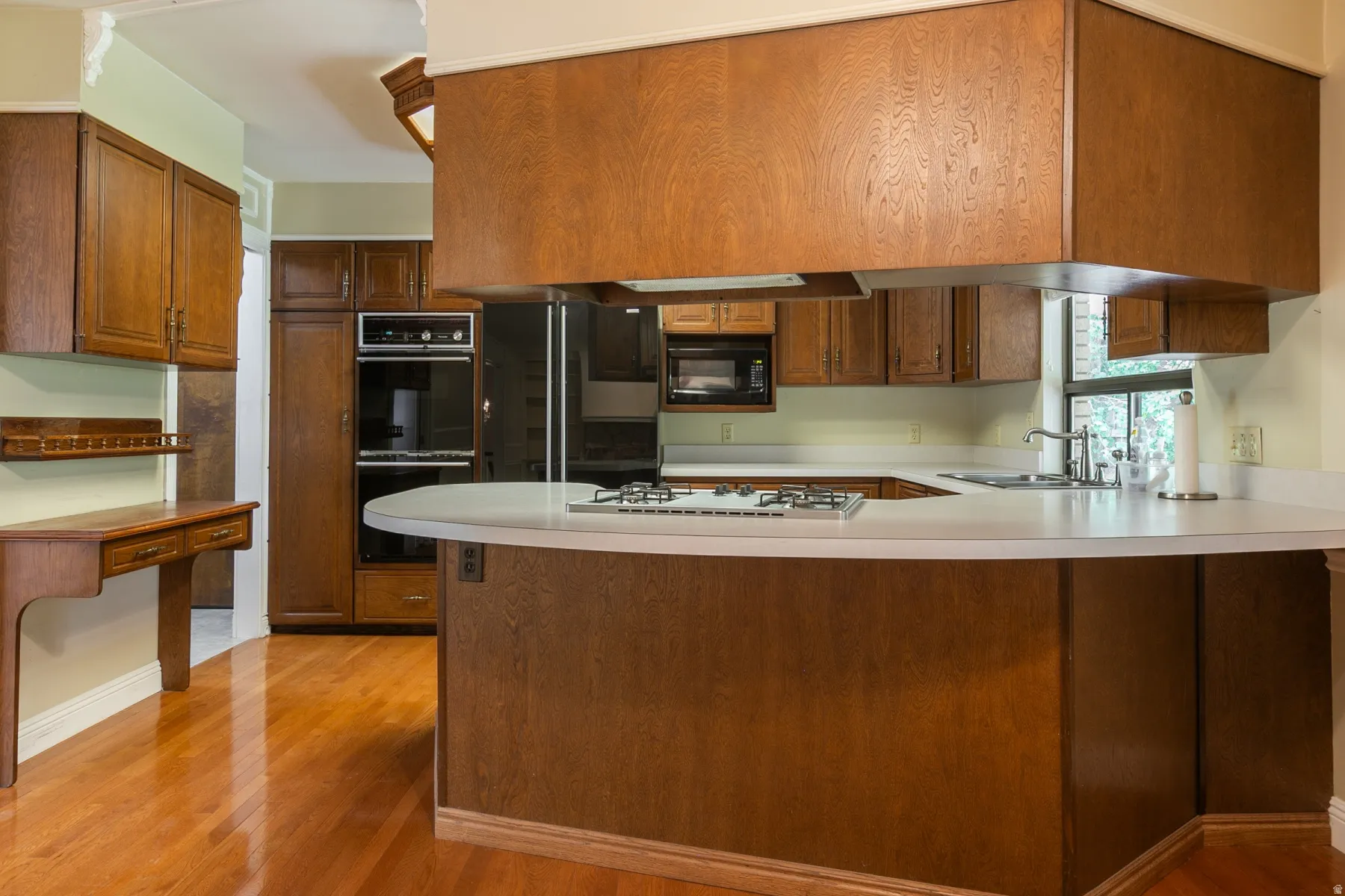 Chef's kitchen featuring rich wood cabinetry, stainless steel appliances including a gas cooktop and built-in wall oven, white quartz countertops, and a curved island with seating