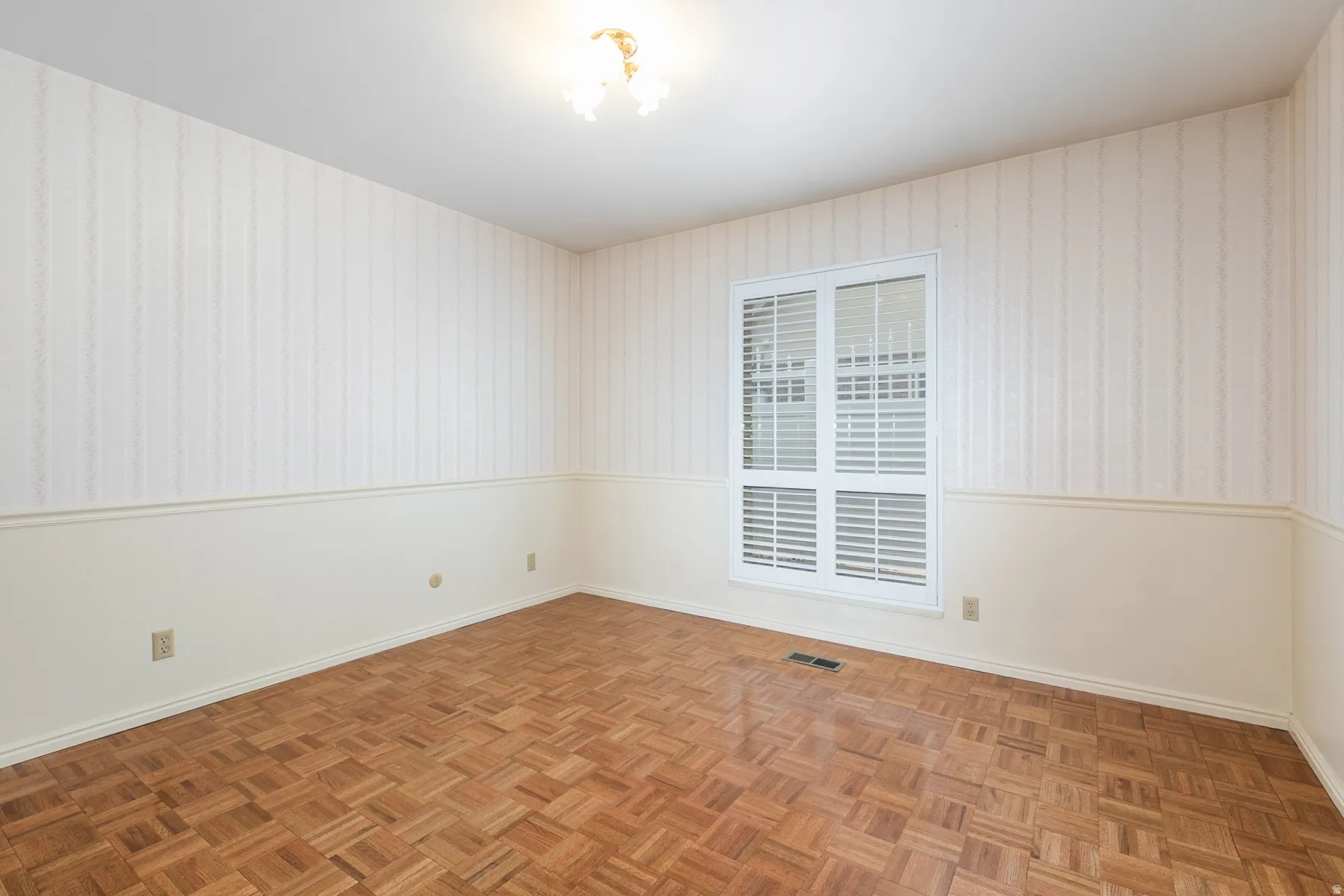 Parquet wood flooring, a window with horizontal blinds, decorative wall paneling, striped wallpaper, and a ceiling-mounted light fixture