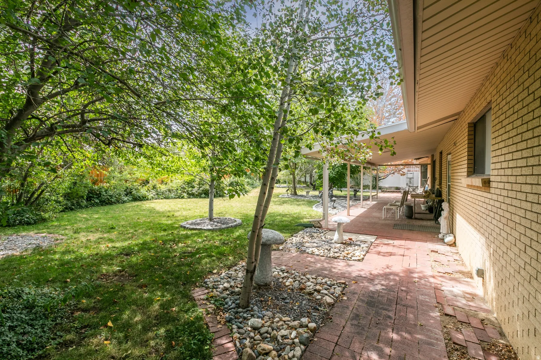 Expansive green lawn, mature trees, brick exterior, covered patio, and brick paver walkway