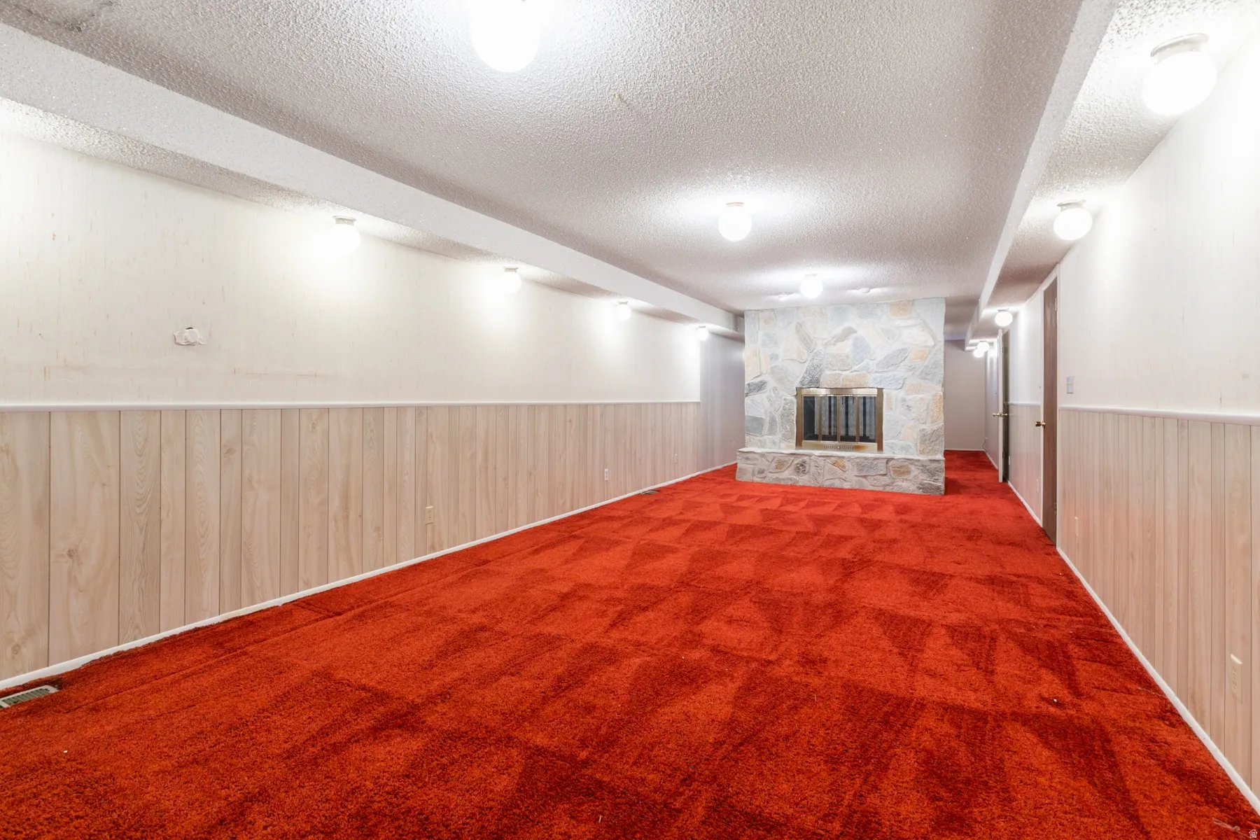 Stone-clad fireplace with a metal insert, red patterned carpeting, and wood-paneled wainscoting