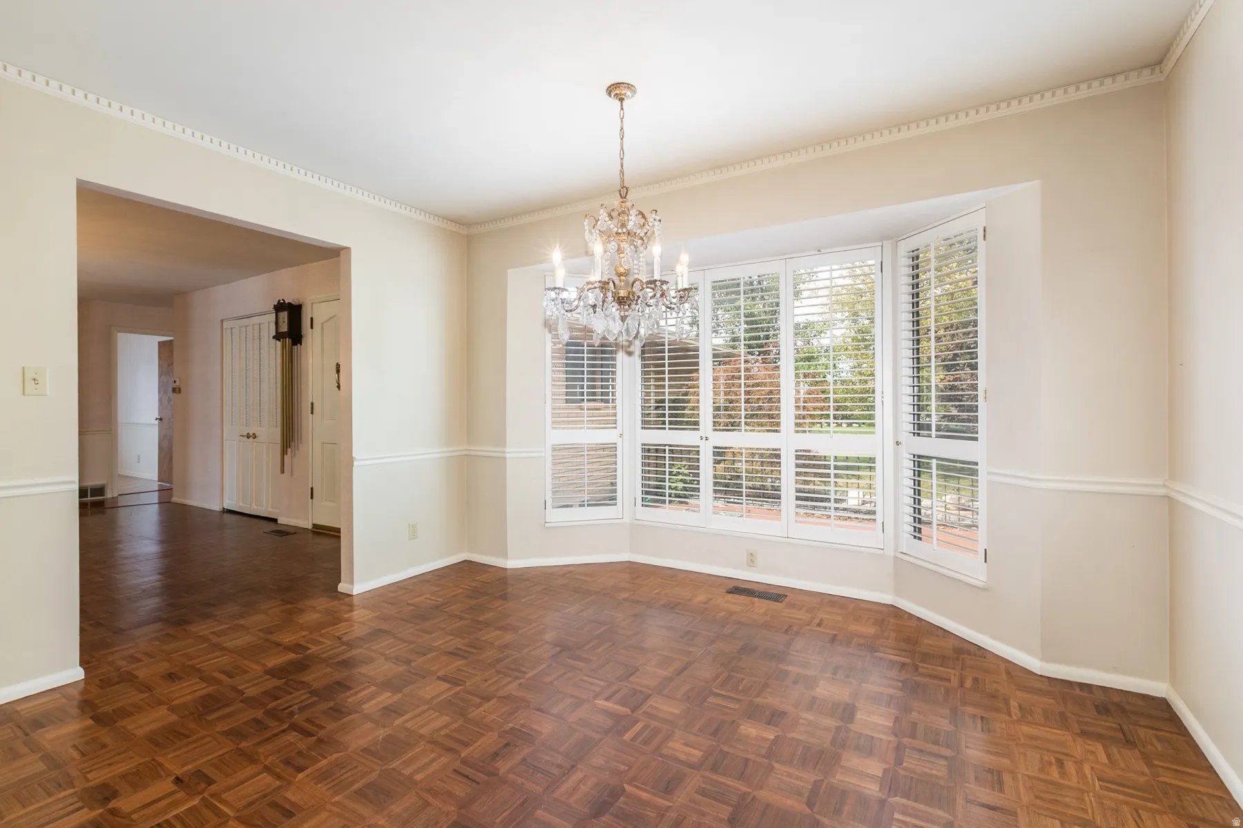 Parquet wood flooring, a crystal chandelier, bay windows with plantation shutters, crown molding, and wainscoting