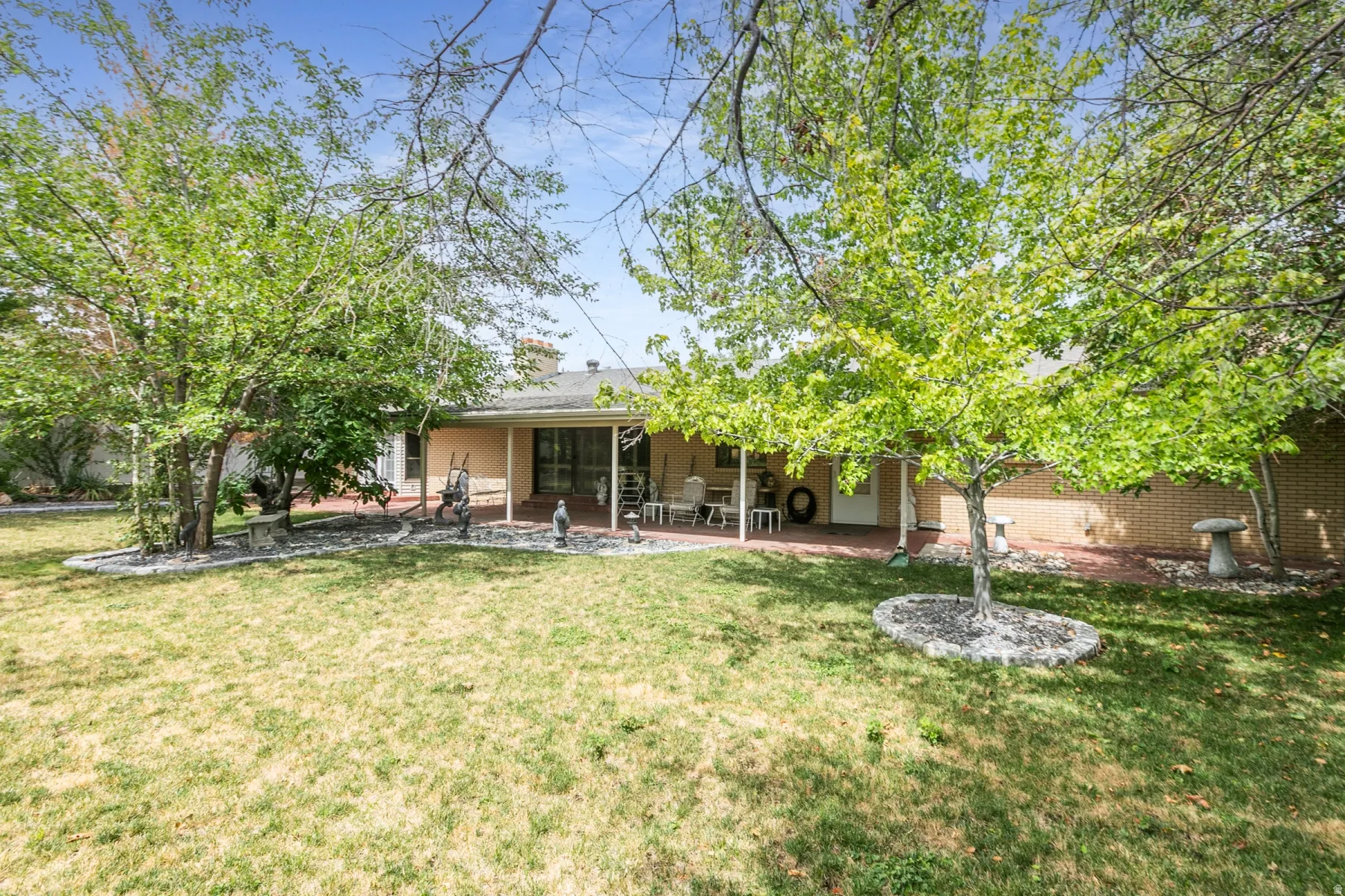Expansive backyard featuring mature trees, a covered patio, brick exterior, and an additional exterior door
