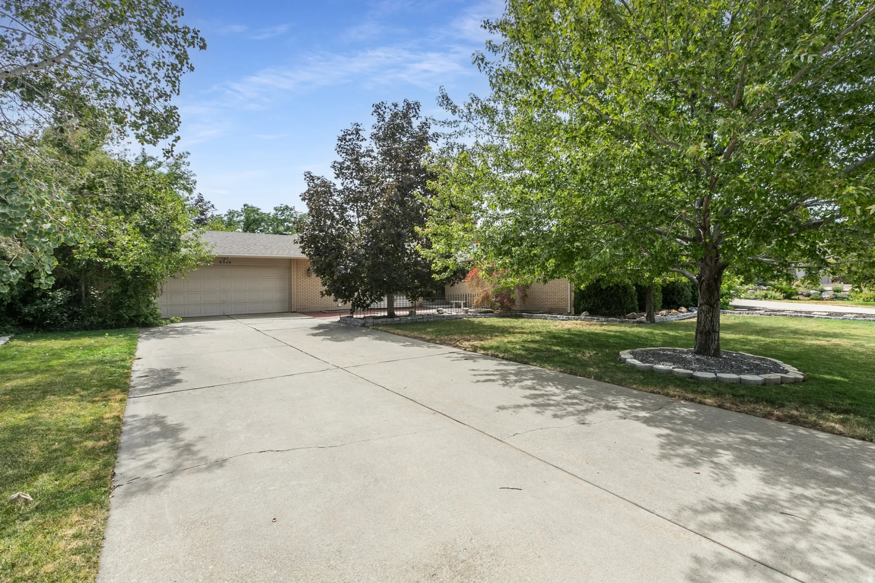 Concrete driveway with a two-car garage, mature trees, and a landscaped front yard