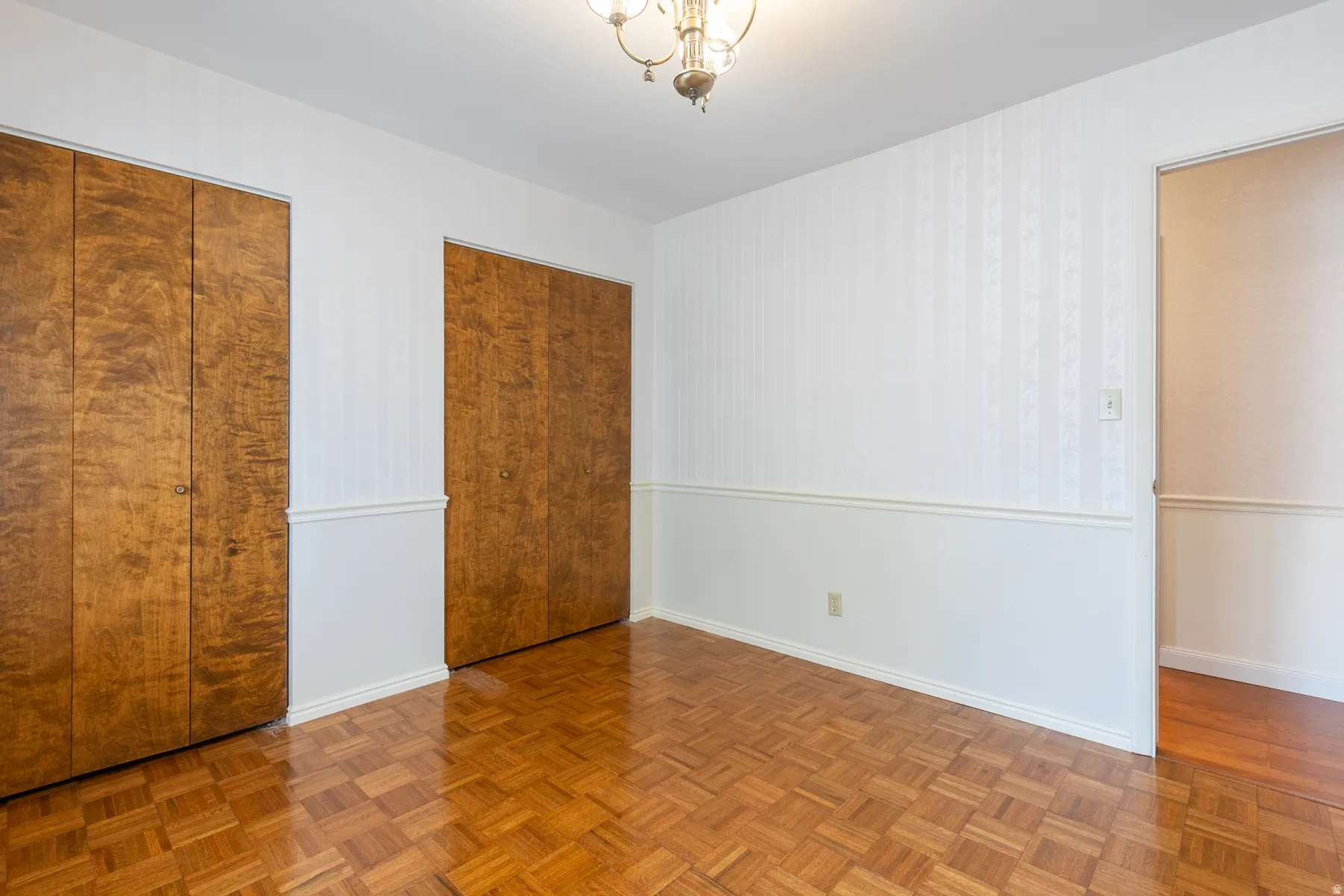 Parquet wood flooring, two wood-finish closets with bifold doors, chair rail molding, and a ceiling-mounted chandelier