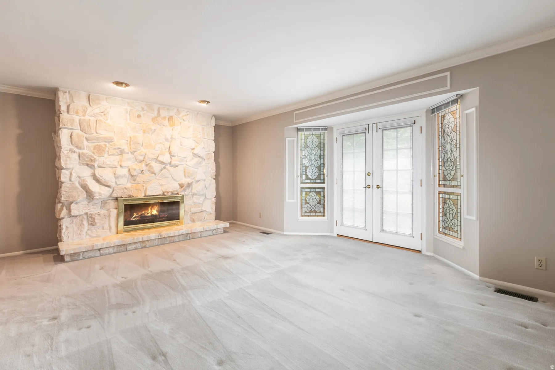 Stone-clad fireplace with a brass firebox, French doors with decorative glass panels, and recessed ceiling lighting