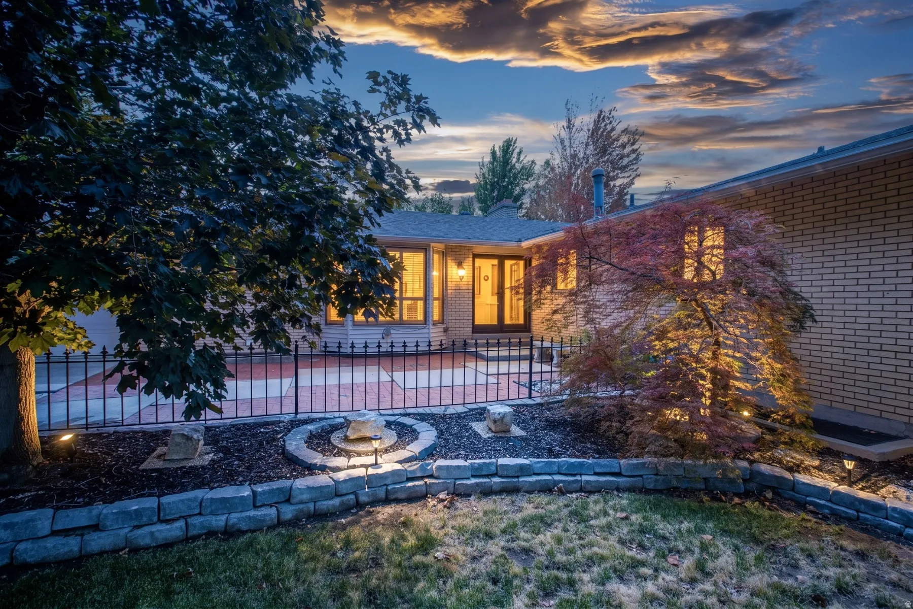 Landscaped exterior featuring a stone retaining wall, decorative rock beds, and mature trees