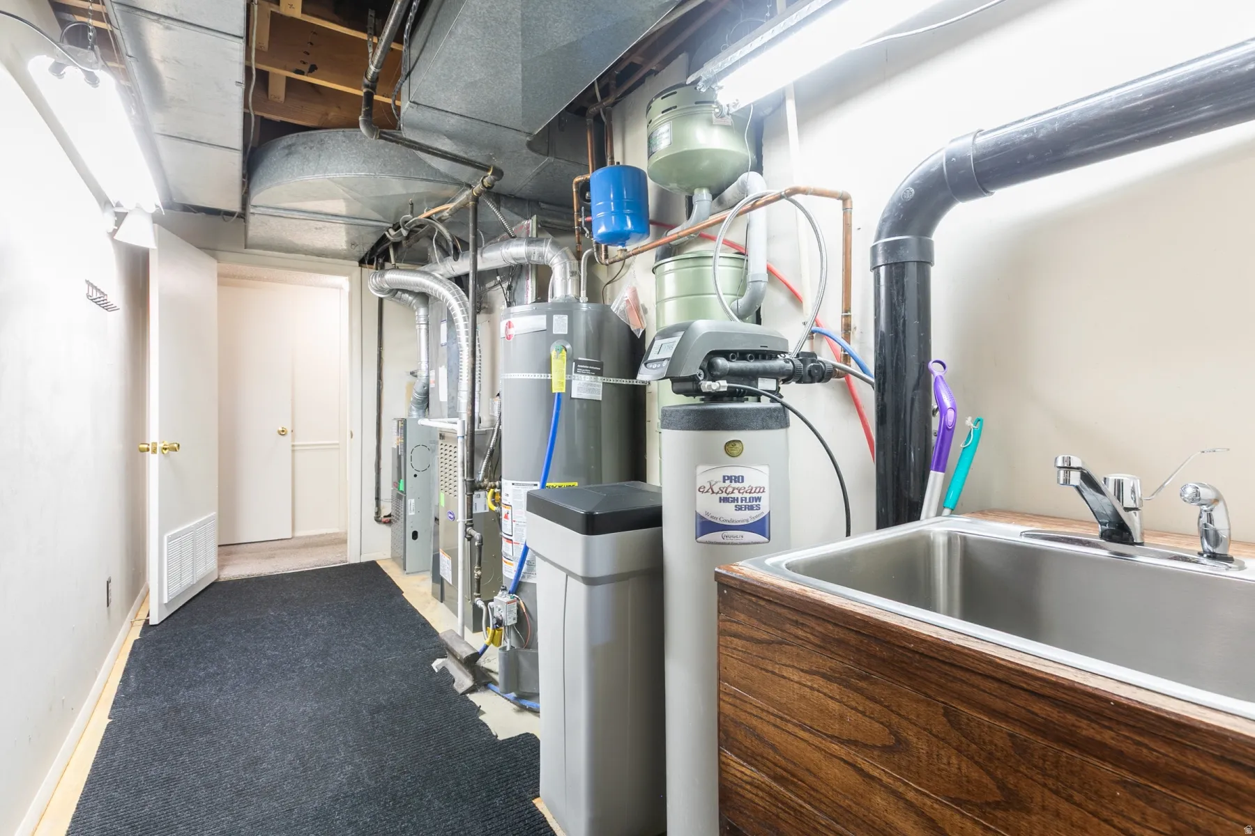 Utility area featuring a stainless steel sink, wood-finish cabinetry, water treatment system, and exposed ductwork