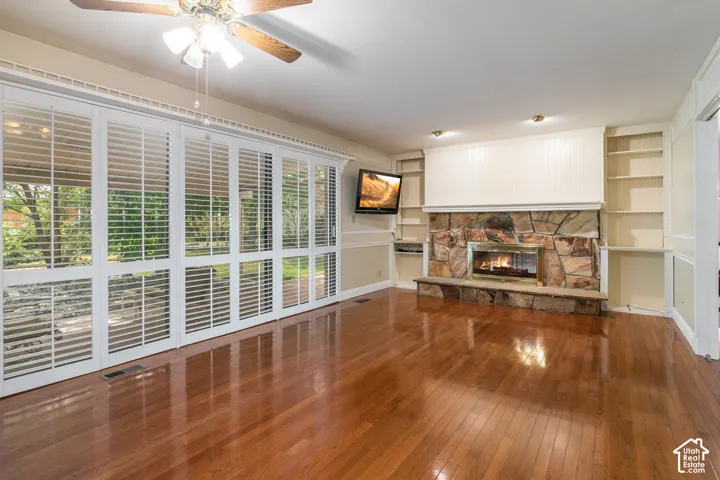 Stone-clad fireplace with built-in shelving, wood-finish flooring, and large windows with plantation shutters