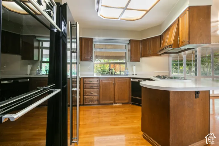 Chef's kitchen showcasing rich wood cabinetry, stainless steel appliances including a professional-style range, white quartz countertops, a curved island with seating, hardwood flooring, and abundant natural light from multiple windows and skylights