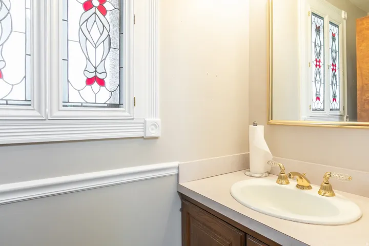 Stained glass windows with ornate trim work, vanity with an integrated sink, gold-tone faucet with crystal handles, and a framed mirror
