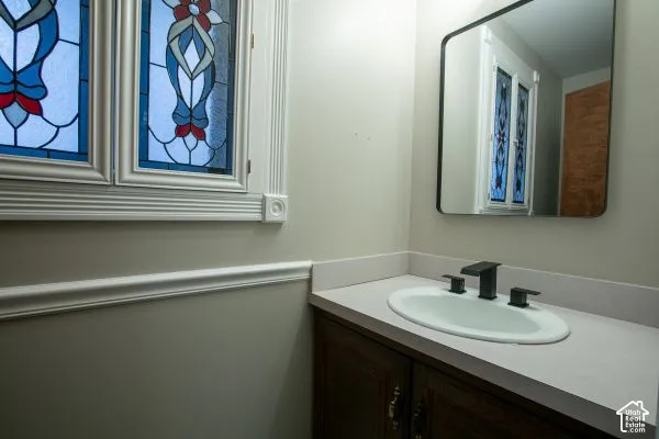 Stained glass window featuring decorative mullions, vanity with solid surface countertop, drop-in sink, matte black widespread faucet, and rectangular wall-mounted mirror