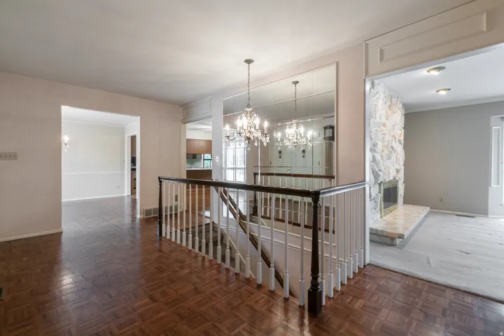 Hardwood parquet flooring, built-in mirror wall, chandelier lighting, staircase with dark wood railing, and a stone-faced fireplace