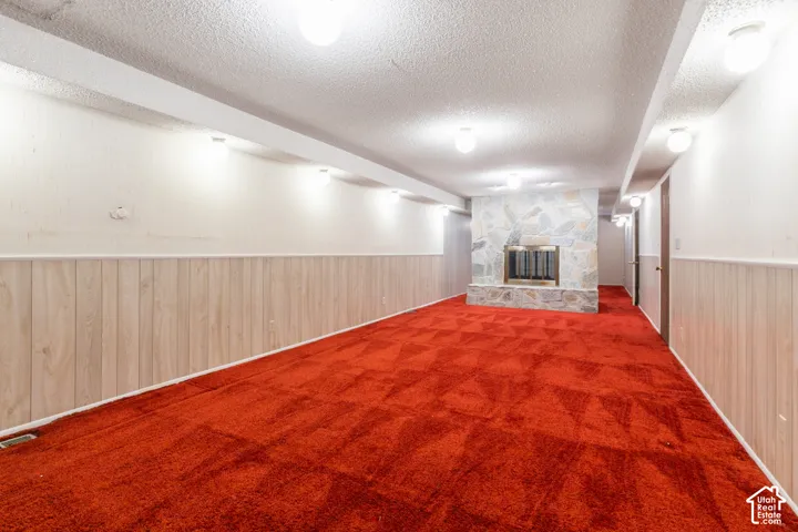 Stone-clad fireplace with a metal insert, red patterned carpeting, and wood-paneled wainscoting