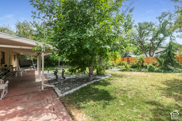 Expansive green lawn with a covered brick patio, mature trees, and a wooden privacy fence
