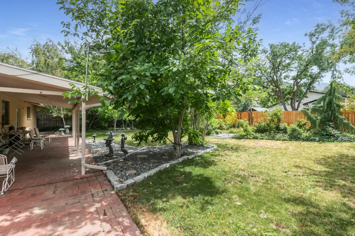 Expansive green lawn with a covered brick patio, mature trees, and a wooden privacy fence